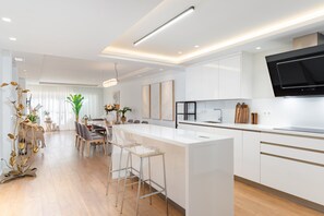 A modern kitchen with white cabinetry, a central island, and a large flat-screen TV mounted above the counter. - GuestReady - Marbella Park (Marbella)