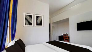 A hotel room with a bed, a flat-screen TV mounted on the wall, and two framed leaf patterns on the wall.