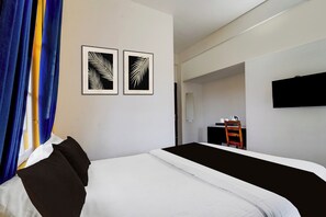 Una habitación de hotel con una cama, un televisor de pantalla plana montado en la pared y dos adornos con motivos de hojas en la pared.