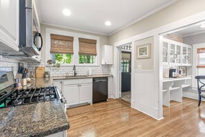A kitchen with white cabinets, a granite countertop, a dishwasher, and a stove. - The Hamilton a Stylish Downtown Bungalow (High Point)