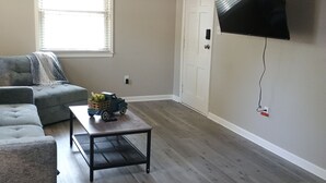 A living room with a grey sofa, a coffee table with a toy truck, a ceiling fan, and a mounted TV. - Cozy home in Ardmore Winston-Salem pet friendly, close to hospital & University (Winston-Salem)