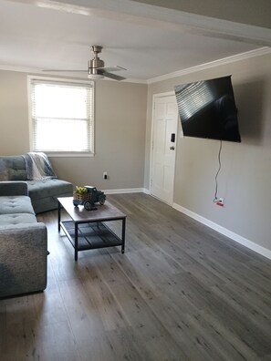 A living room with a grey sofa, a coffee table with a toy truck, a ceiling fan, and a mounted TV. - Cozy home in Ardmore Winston-Salem pet friendly, close to hospital & University (Winston-Salem)
