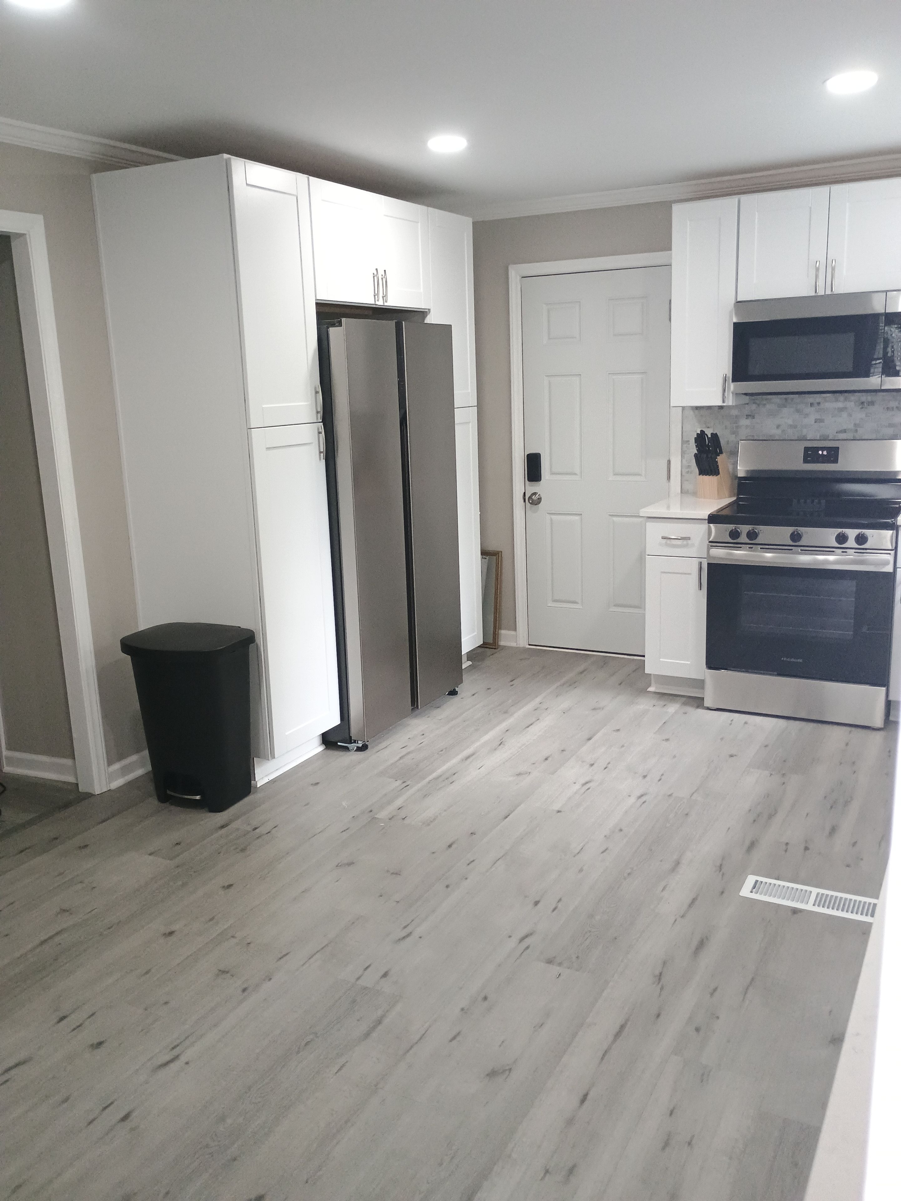 A kitchen with white cabinets, a stainless steel refrigerator, a black stove, and a trash bin.