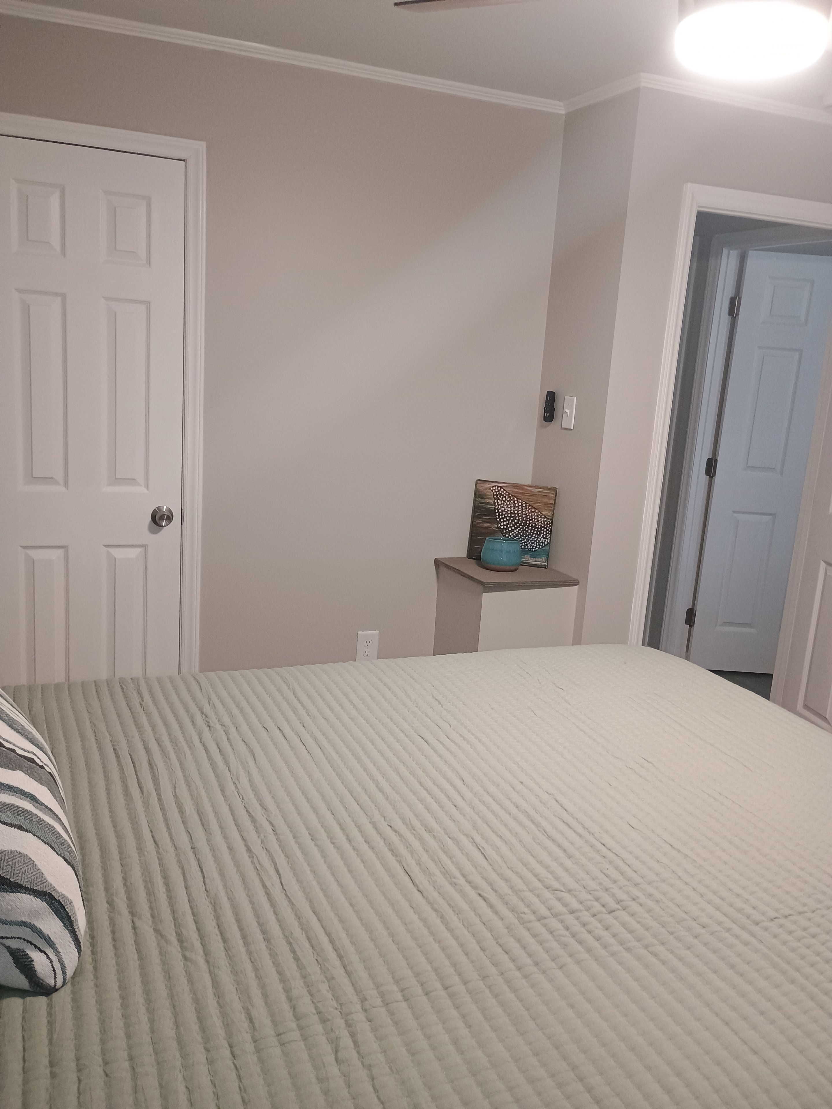 A bedroom with a bed, a door, a nightstand, and a wall-mounted light fixture.