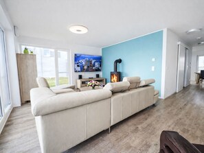 Een moderne woonkamer met een hoekbank, een open haard en een aan de muur bevestigde televisie.