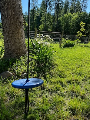 Un objet bleu suspendu dans un espace extérieur verdoyant, avec un arbre et une clôture en arrière-plan.