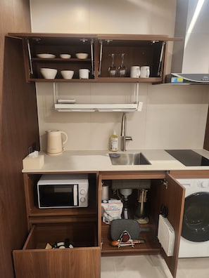 A compact kitchen with a microwave, sink, and a washing machine.