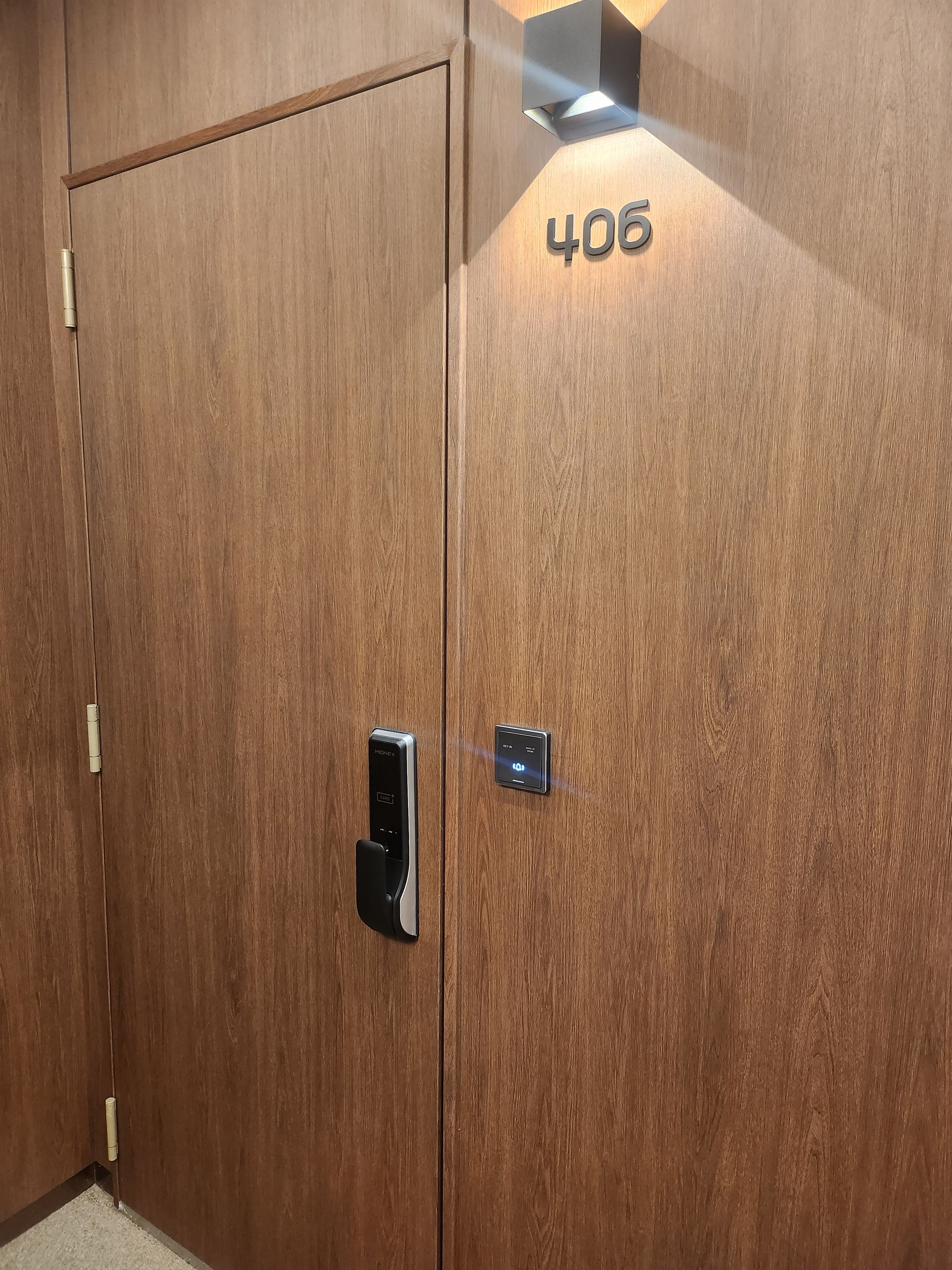 Een houten deur met een digitaal slot en het getal '406' op de muur.
