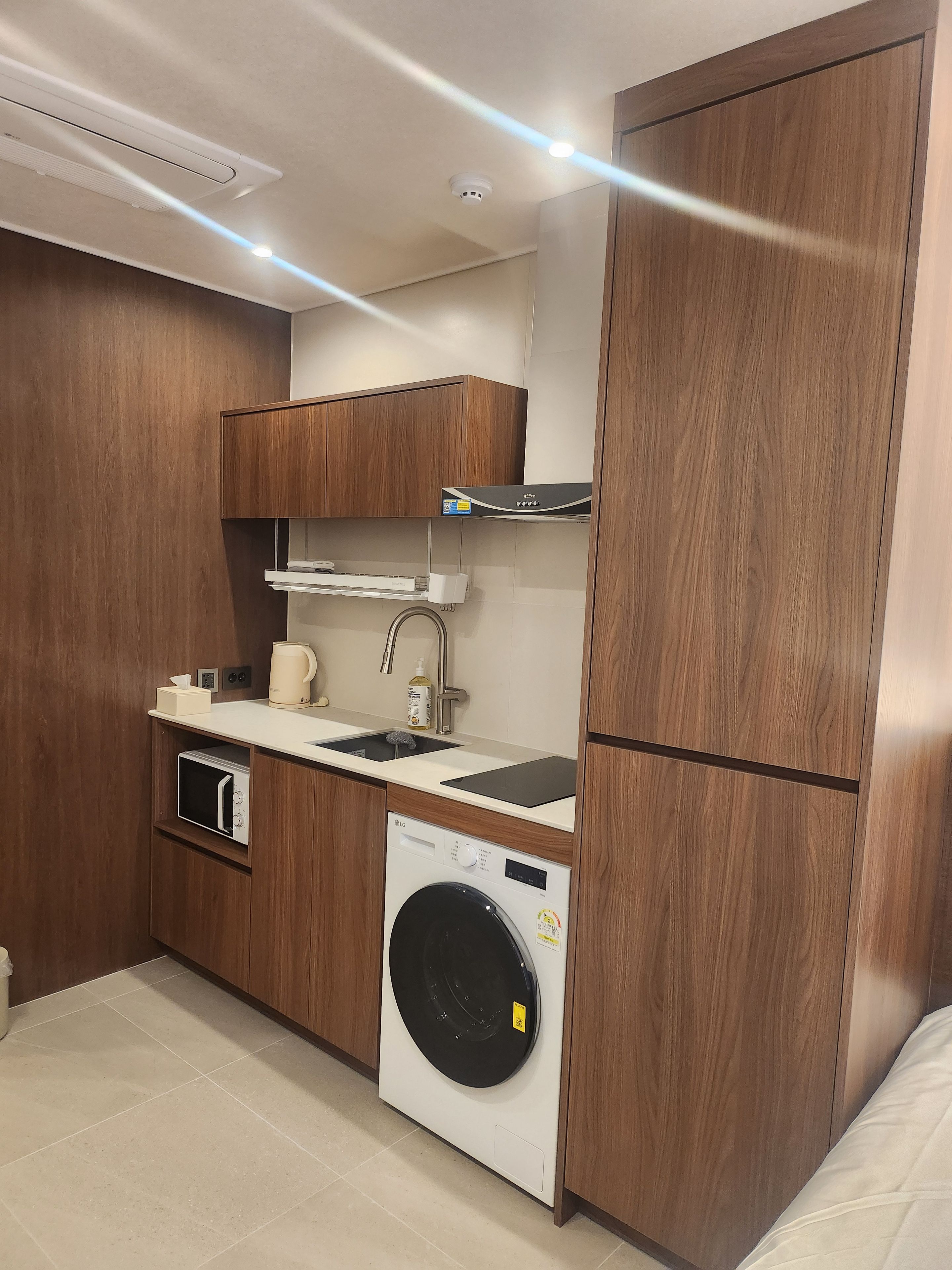 Cocina compacta con armarios de madera, lavadora integrada, cafetera y un lavabo.