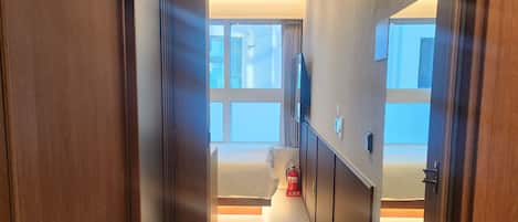 Un pasillo que lleva a un dormitorio con cama, televisor y extintor.