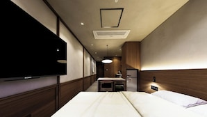 Ein Hotelzimmer mit Bett, Flachbildfernseher an der Wand, Schreibtisch mit Stuhl und integriertem Kleiderschrank.