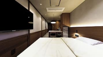 A hotel room with a bed, a flat-screen TV mounted on the wall, a desk with a chair, and a built-in wardrobe.