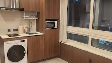 A compact kitchen with a washing machine, microwave, and built-in oven.