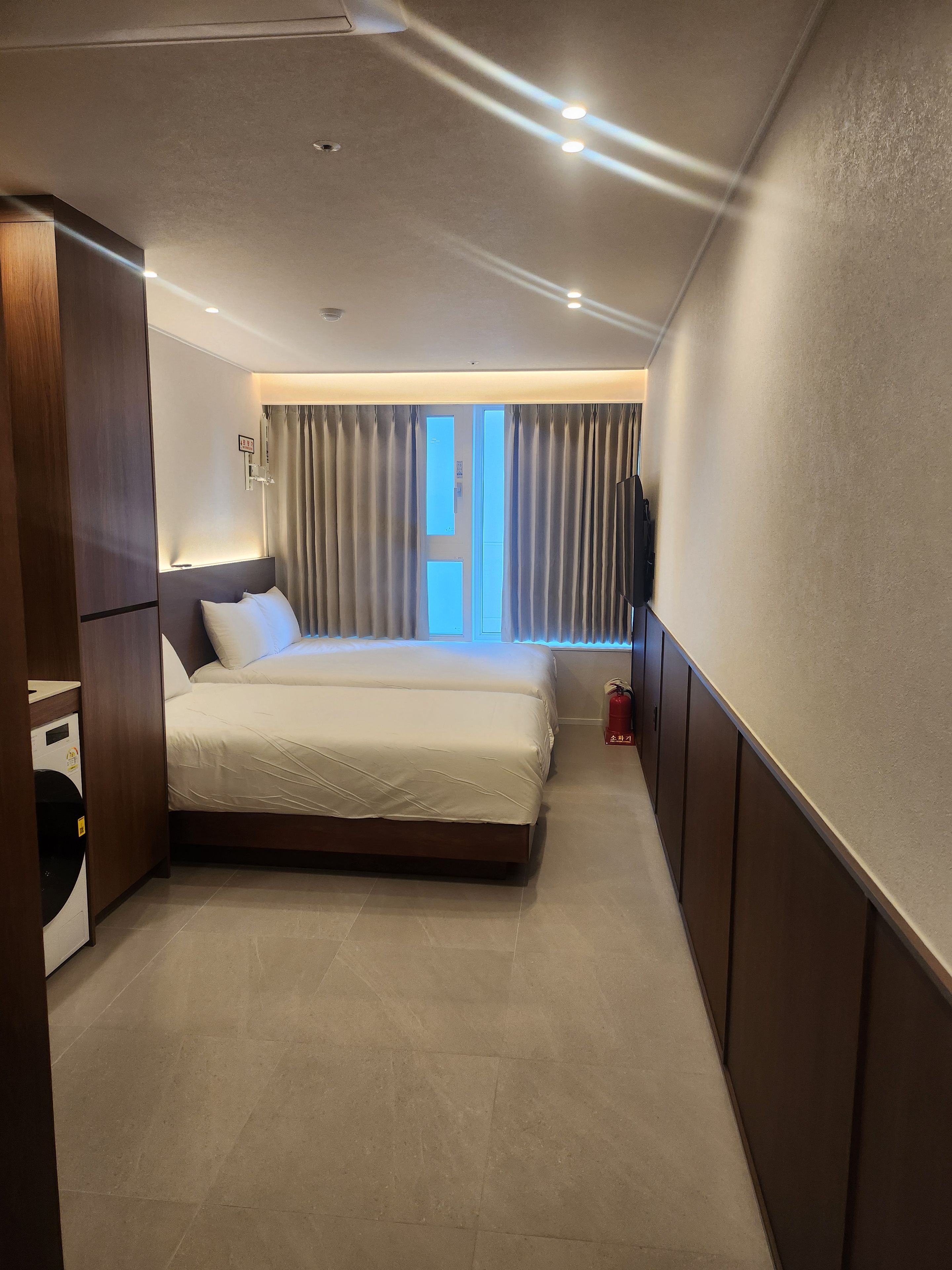 Una habitación de hotel con una cama, un televisor, una ventana con cortinas y un extintor.