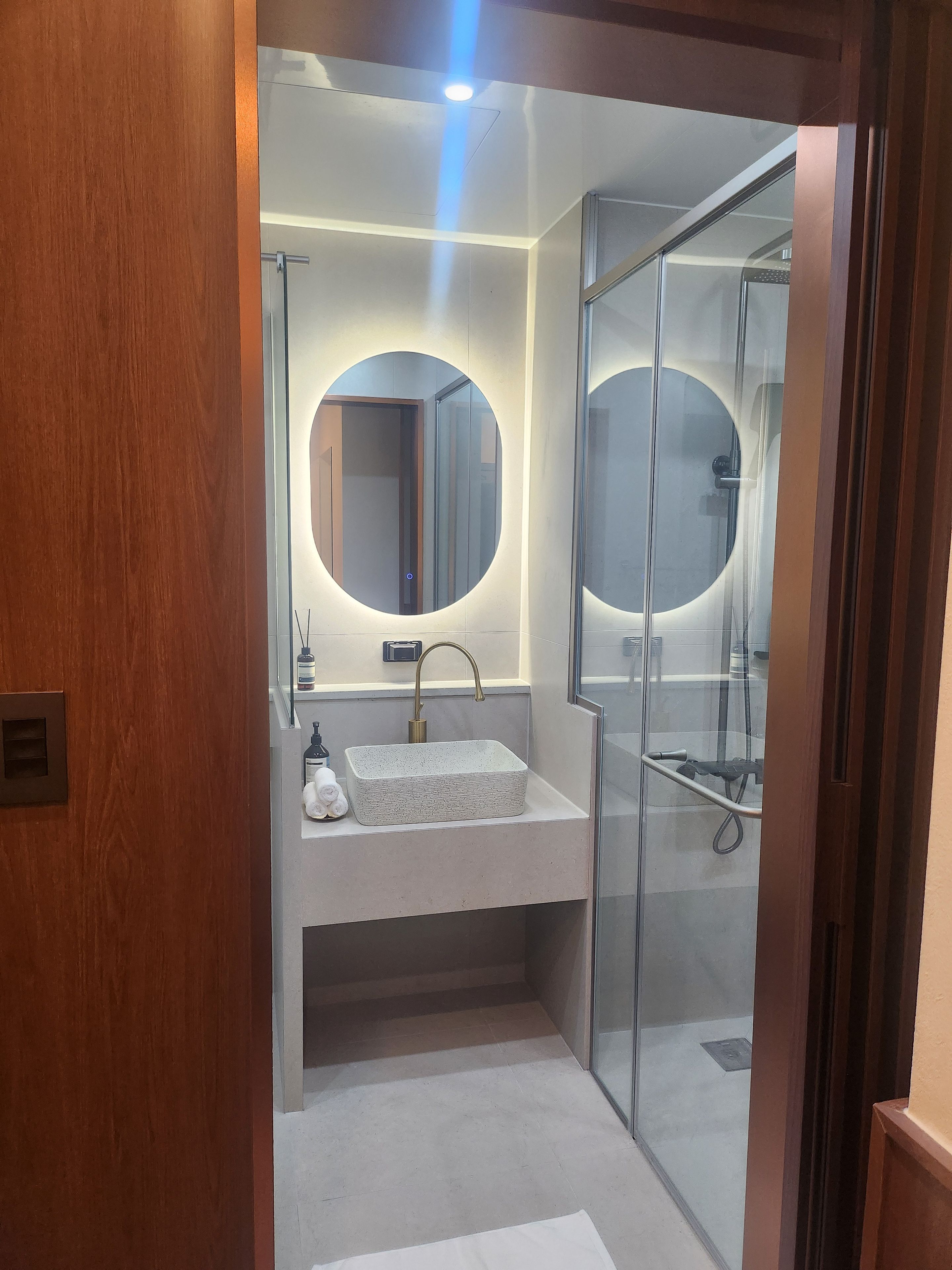 Un baño moderno con cabina de ducha de vidrio, un espejo redondo y un lavabo rectangular.