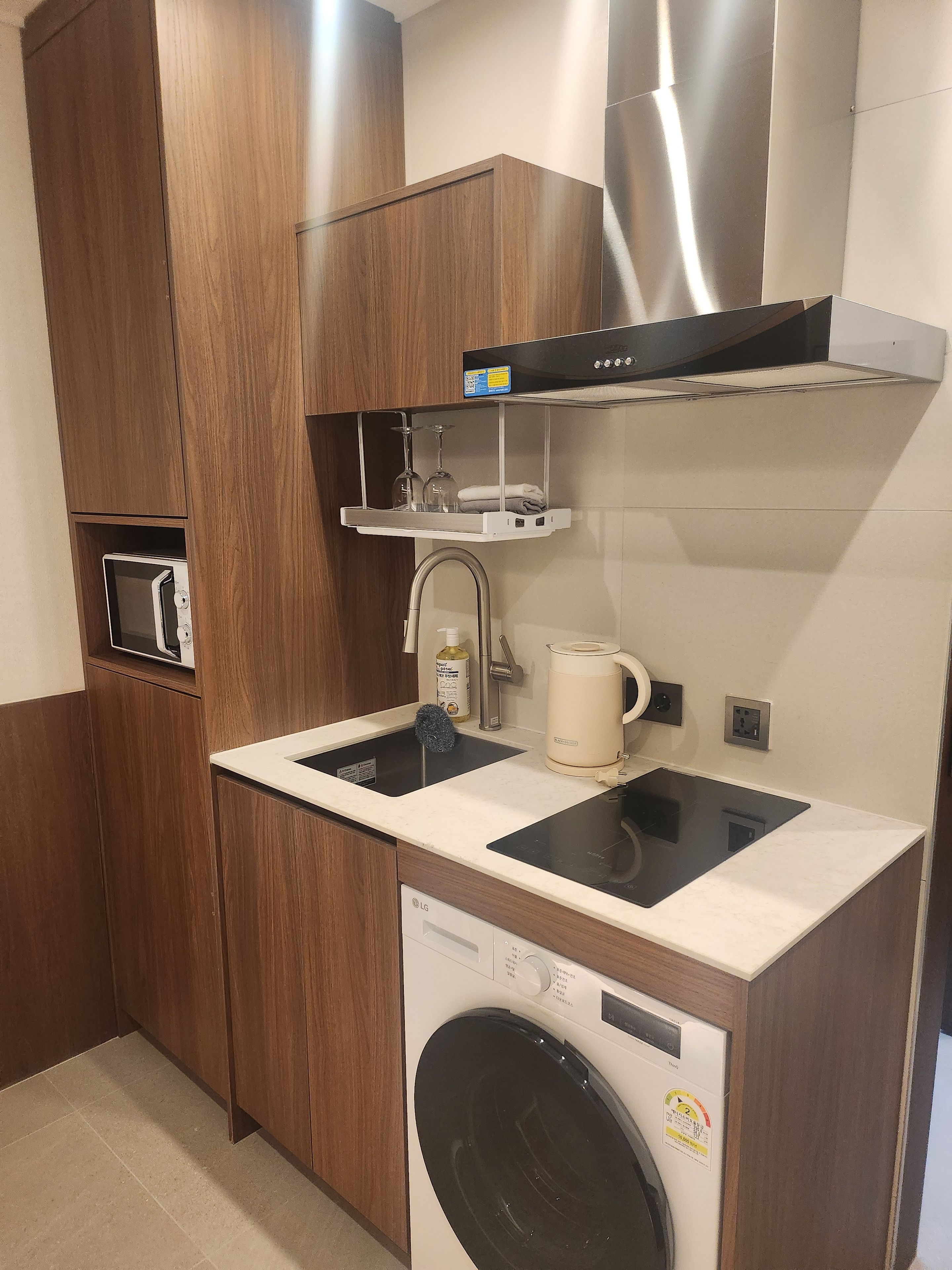 Een functionele keuken met een inbouw wasmachine, een magnetron en een roestvrijstalen afzuigkap.