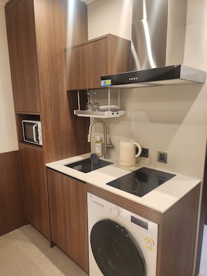 A compact kitchen with a built-in washing machine, a microwave, and a stainless steel range hood. - THE DH STAY (Seoul)