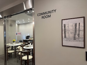 A community room with a clock, caution glass sign, and a framed black and white drawing on the wall.