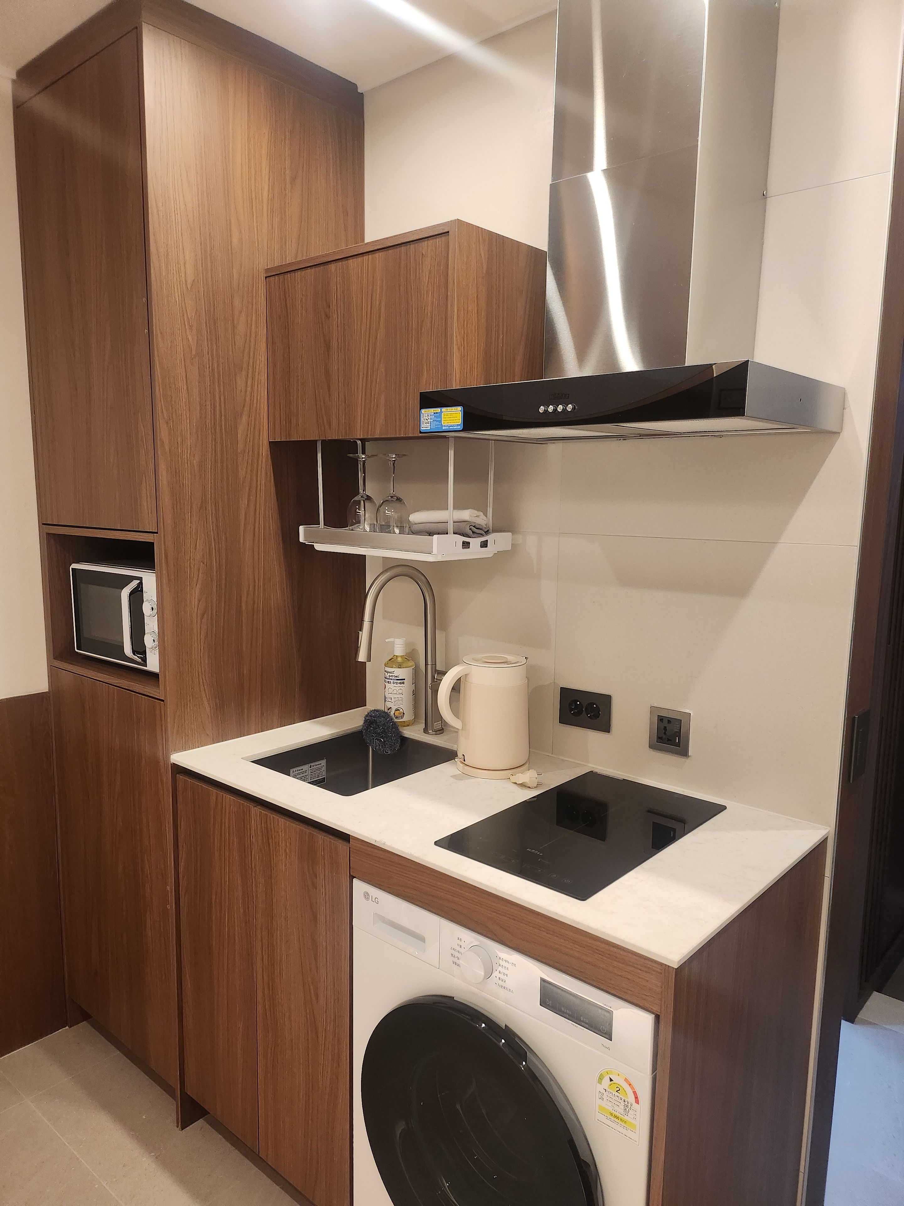 Een praktische keuken met houten kastjes, een roestvrijstalen afzuigkap, een magnetron, een koffiezetapparaat en een ingebouwde wasmachine.
