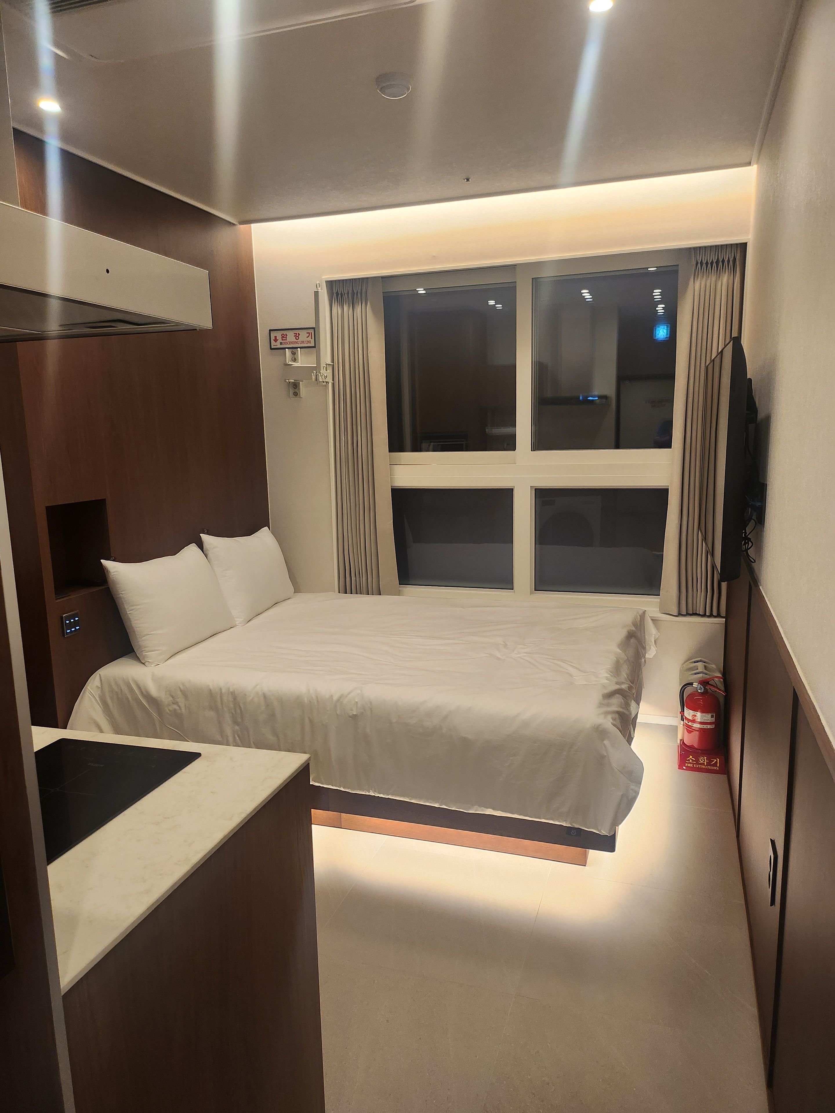 A hotel room with a bed, a bedside table, a television, and a window with curtains.