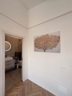 A hallway with a modern bathroom, a wall-mounted artwork, and a wooden floor. - Cozy 1-bedroom apartment in northside Bucharest with AC and terrace (București)