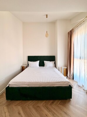 A large bed with a dark headboard, two bedside tables, and a hanging light fixture. - Cozy 1-bedroom apartment in northside Bucharest with AC and terrace (București)