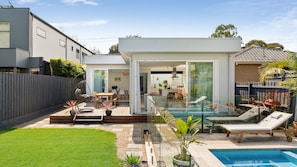 Una casa moderna con piscina, un patio amueblado y un jardín trasero cercado.