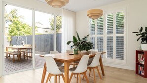A dining area with a wooden table and white chairs, a potted plant, and a bookshelf with books. - Mira Sol, Richmond Hosted by L'Abode Accommodation (Richmond)
