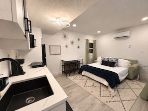 Quarto moderno com cama, escrivaninha e cozinha compacta.