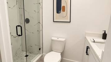 Un baño moderno con cabina de ducha de vidrio, inodoro y lavabo con encimera.