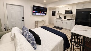 A modern hotel room with a bed, a TV, a kitchenette, and a door. - Stadium Nest /king Bed/ pet friendly (Tampa)