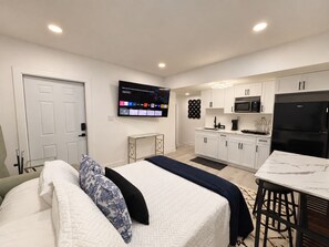 Quarto de hotel moderno com cama, televisão, cozinha compacta e porta.