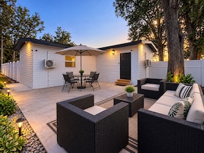 Uma área de pátio com móveis de exterior, uma mesa e cadeiras, e um espaço de estar coberto.