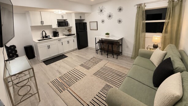 A modern kitchen with white cabinets, a black refrigerator, and a dining area with a table and chairs. - Stadium Nest /king Bed/ pet friendly (Tampa)