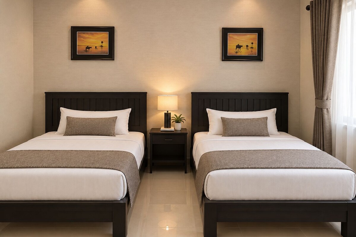A hotel room with two beds, a nightstand with a lamp, and two framed pictures on the wall.