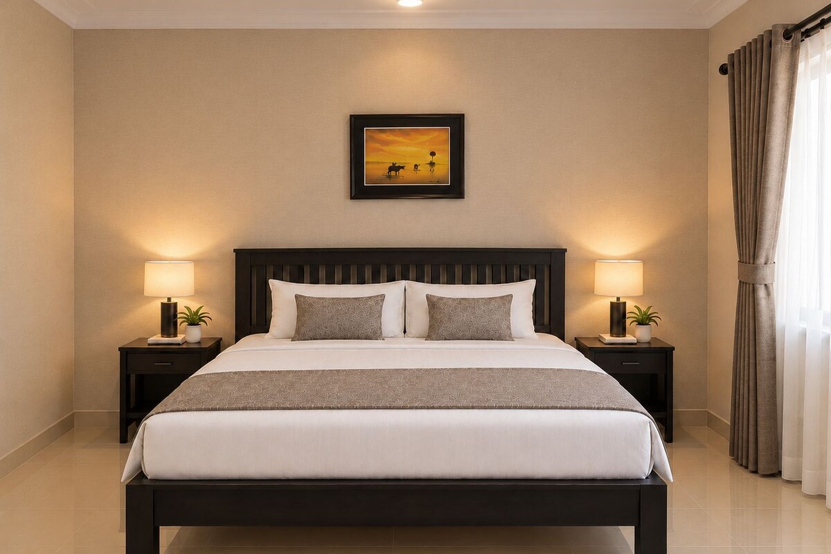 A hotel room with a large bed, two bedside tables with lamps, a framed picture on the wall, and a window with curtains.
