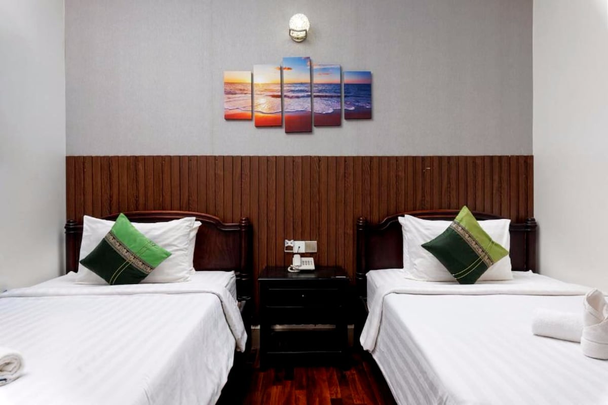 Ein Hotelzimmer mit zwei Betten, einem Nachttisch mit Telefon und einem an der Wand hängenden Kunstwerk darüber.