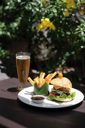 A meal consisting of a burger, fries, and a glass of beer on a white plate, with a green plant in the background. - Central Boutique (Siem Reap)