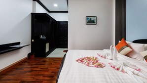 Une chambre d’hôtel avec un lit, un tableau au mur, une armoire noire et un plancher en bois.