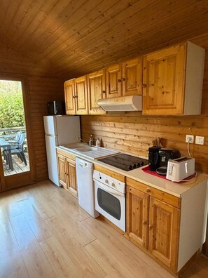 A compact kitchen with wooden cabinets, a built-in oven, a sink, and a coffee maker. - LE CHAMOIS No. 8 - A 6-person chalet surrounded by nature, lakes, and waterfalls in the Jura (Uxelles)