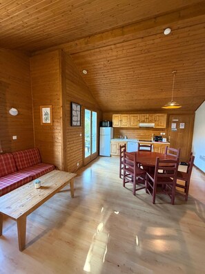 A wooden interior with a dining table and chairs, a sofa, and a kitchen area. - LE CHAMOIS No. 8 - A 6-person chalet surrounded by nature, lakes, and waterfalls in the Jura (Uxelles)