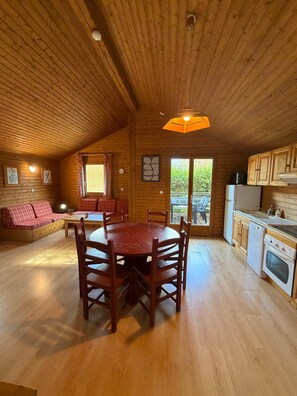 Interior em madeira com mesa de jantar, cadeiras, sofá e área de cozinha.