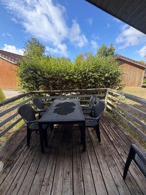 Um deck de madeira ao ar livre com mesa e cadeiras, cercado por uma cerca de madeira e um hedge.