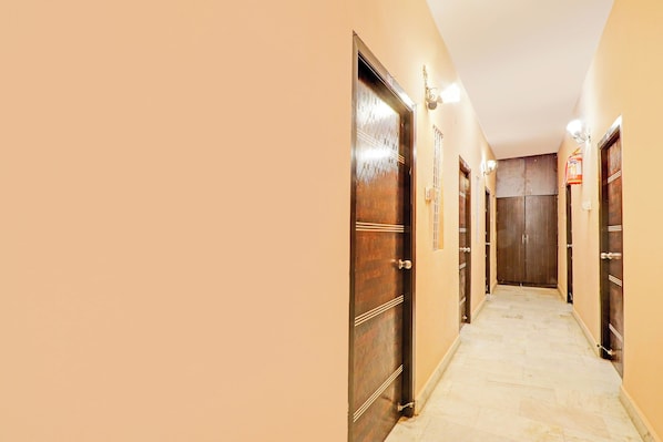 A corridor with wooden doors, a fire extinguisher, and a light fixture on the wall. - Hotel O Karimnagar (Karimnagar)
