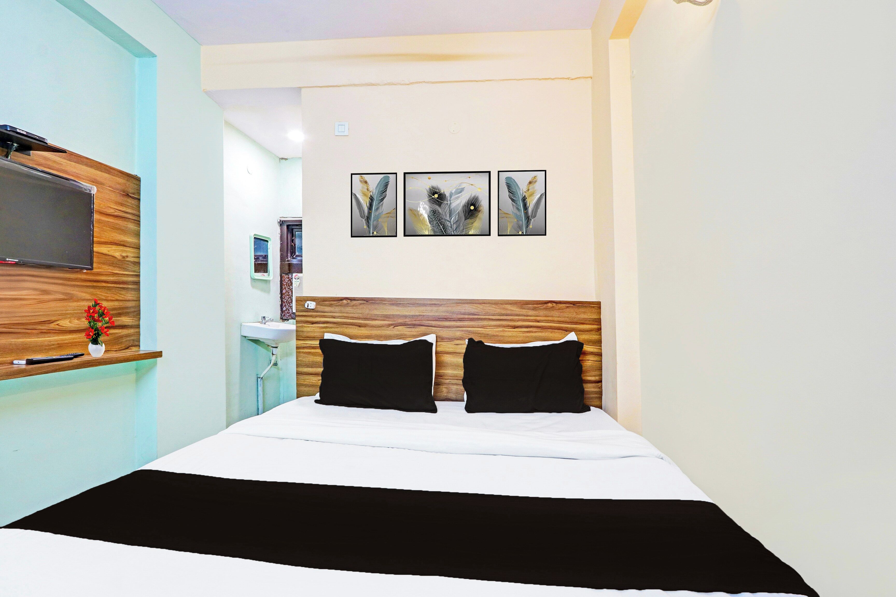A hotel room with a bed, a TV mounted on the wall, a small desk with a computer, and a window.
