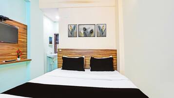 A hotel room with a bed, a TV mounted on the wall, a small desk with a computer, and a window.