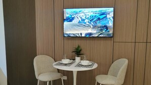 Habitació d'hotel amb un llit, una taula petita rodona amb dues cadires, una televisió penjada a la paret i una planta en test.