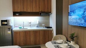 Habitació d'hotel senzilla amb cuineta, zona de menjador amb taula i cadires, llit amb edredó blanc i televisió penjada a la paret.