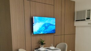 Habitació d'hotel moderna amb televisió de pantalla plana penjada a la paret, taula rodona de menjador amb dues cadires i llit amb roba de llit blanca.