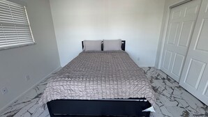 Una camera da letto con un letto, una finestra con persiane, una porta e un pavimento effetto marmo.
